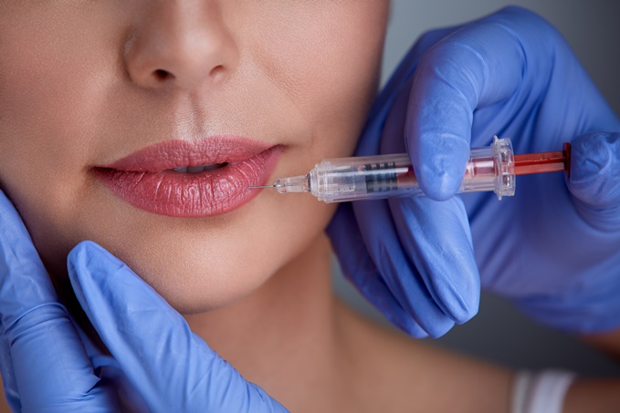 Mão com luvas aplicando botox perto do lábio de uma mulher